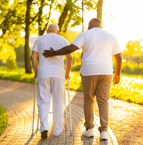 Back photo of elderly man walking with walker with his caregiver